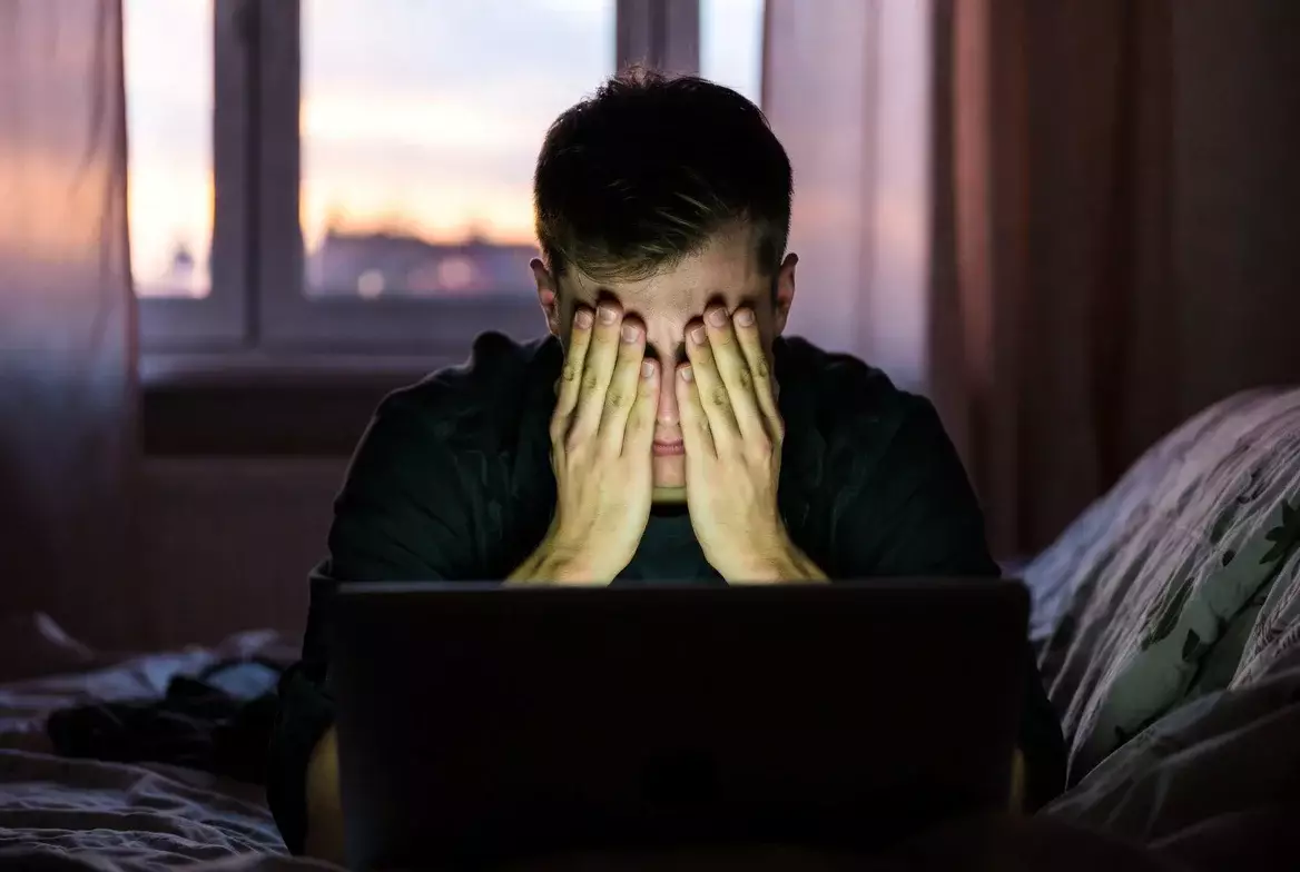 Persona frustrata con le mani sul viso davanti al laptop