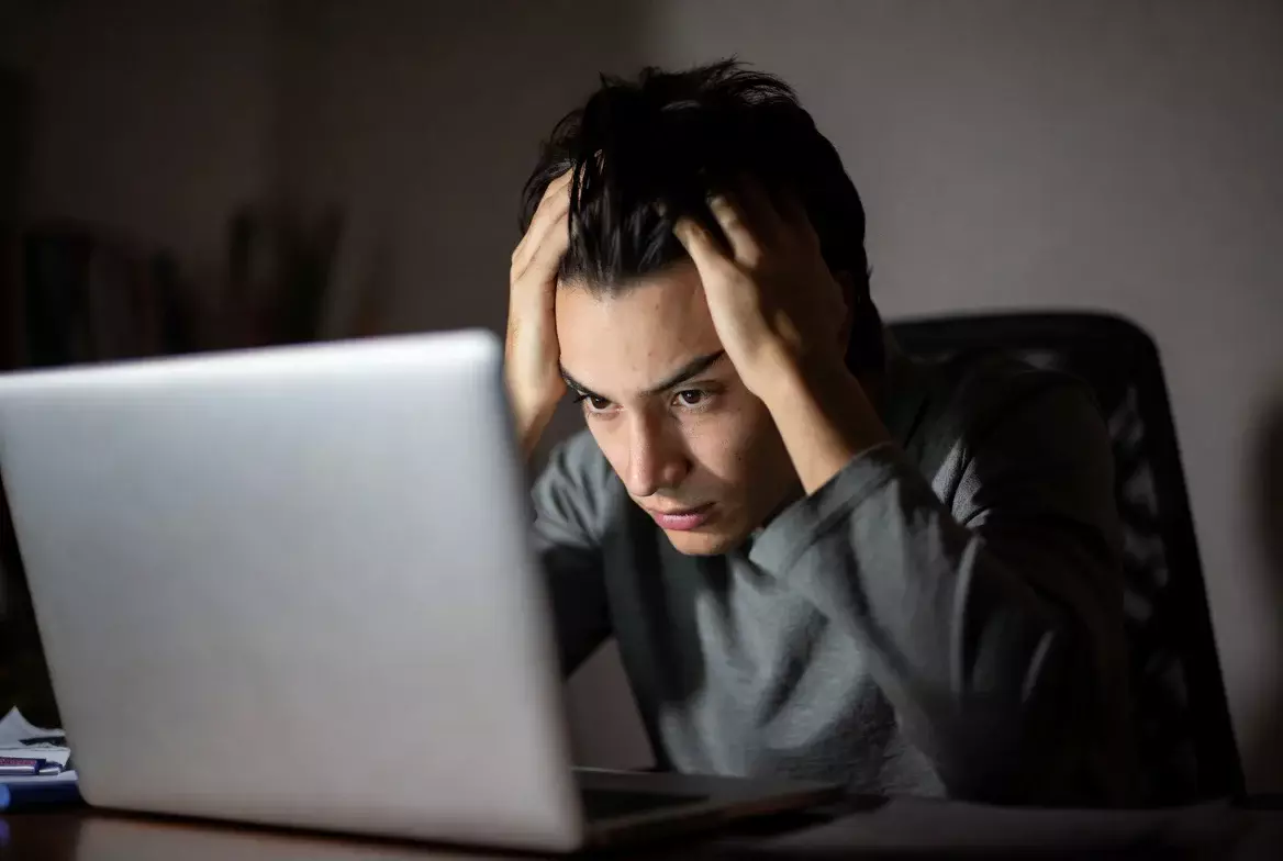 Persona preoccupata che si tiene la testa tra le mani alla scrivania