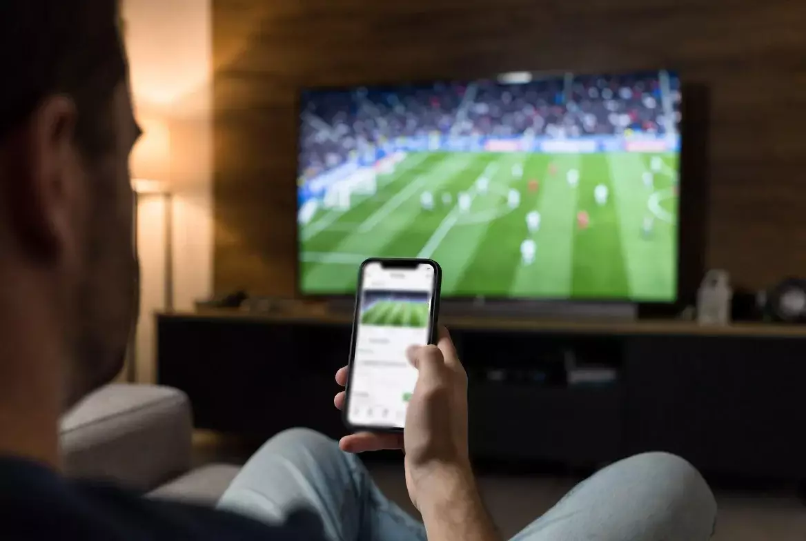 Persona che guarda una partita di calcio mentre consulta lo smartphone