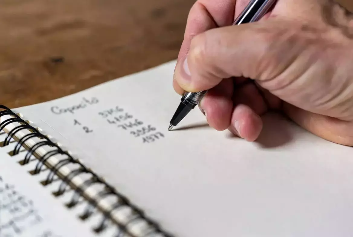 Mano che scrive numeri su un quaderno con penna